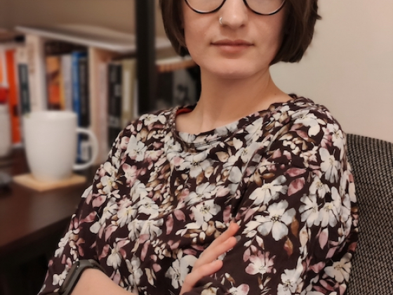 woman in glasses sitting in a chair with arms crossed in front of a bookcase